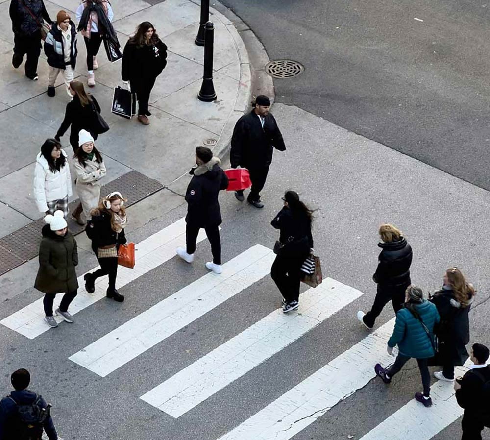 Aerial view of a busy pedestrian crosswalk with people in winter clothing walking in various directions.