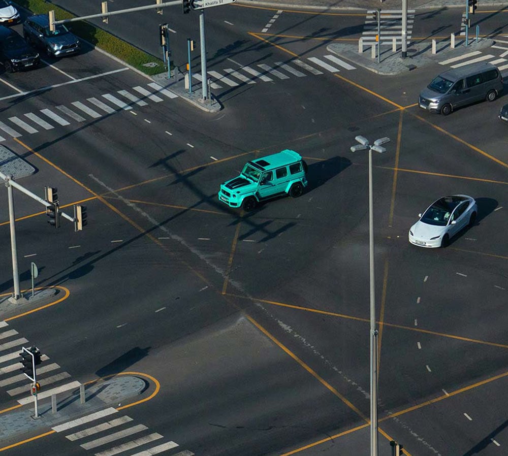 Aerial view of a large intersection with multiple lanes, crosswalks, traffic lights, and moving vehicles.
