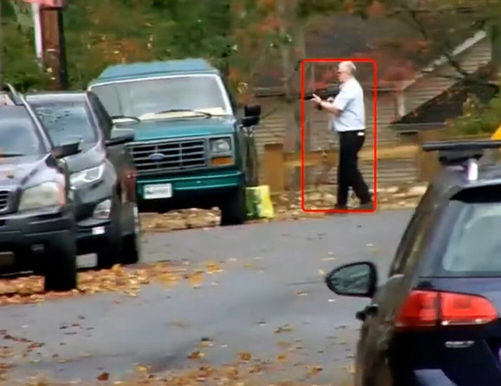 Man in light shirt holding a firearm on a residential street, walking while aiming. Highlighted in red box.